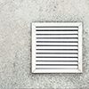 Aged vent with white shutters on the background of gray concrete under the leaves of the palm.